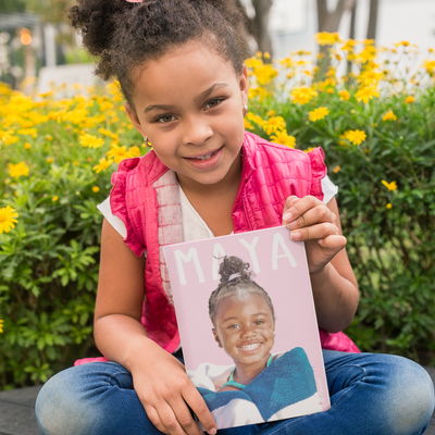 Cute little girl holding her custom kid poster on pink background
